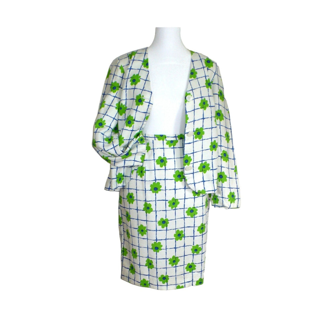 A two-piece skirt suit set featuring a white skirt and matching open-front jacket, both decorated with a blue grid pattern and green shamrock motifs, displayed on a white mannequin torso.