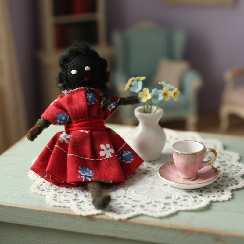 1950s American Folk Art Bendy Doll Pocket Posie. - Small black doll in a red dress on a table with a cup and flowers.