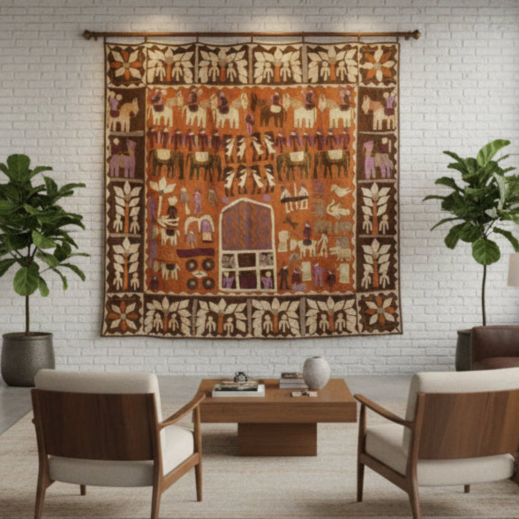 A20th-century Indian Kanduri shrine cloth featuring a detailed tribal-style scene with animals and geometric motifs, hanging on a white brick wall above a wooden coffee table and two armchairs in a modern living room setting.