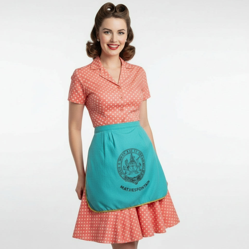 Woman wearing a vpolka dot dress and a 950s Vintage Teal Matjiesfontein South Africa Souvenir Apron on a white background.
