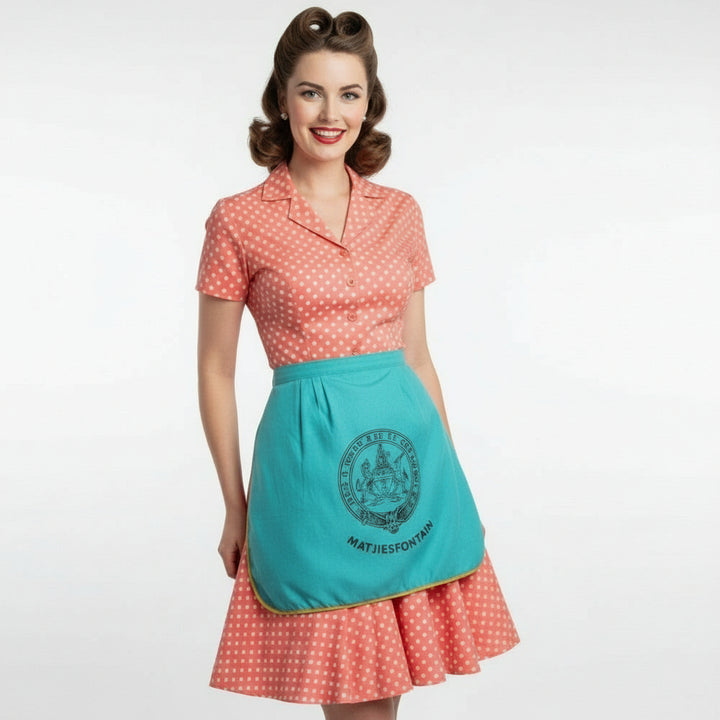 Woman wearing a vpolka dot dress and a 950s Vintage Teal Matjiesfontein South Africa Souvenir Apron on a white background.