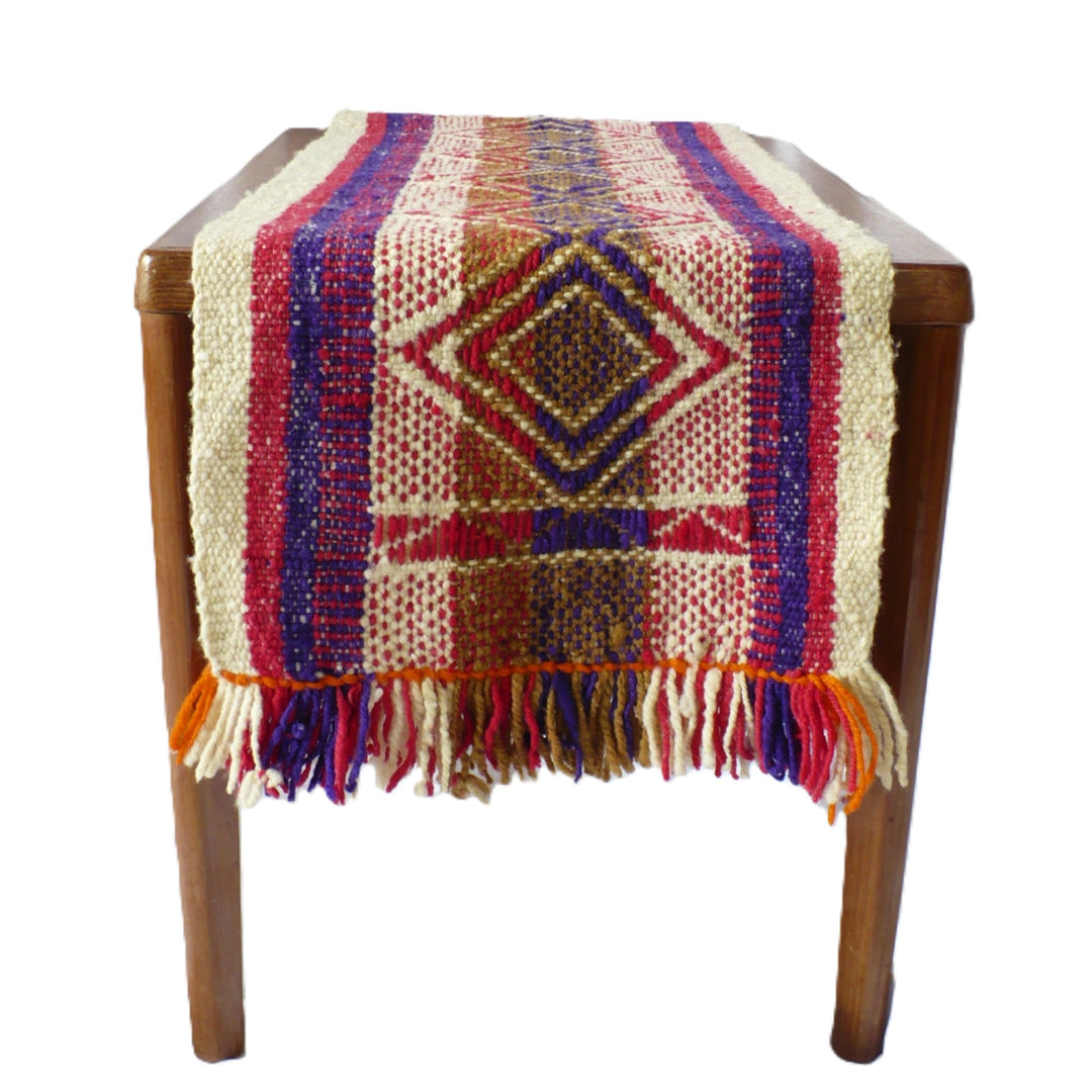 A 1960s Handwoven Mapuche Table Runner (38-inches) - Argentina, woven table runner with a geometric diamond pattern in cream, red, blue, brown, and orange, draped over a wooden table against a white background.