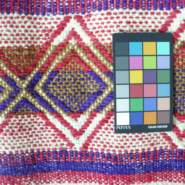 A close-up of a 1960s Handwoven Table Runner (38-inches) - Argentina  featuring a Pleyss color checker card placed on the right side for color reference.