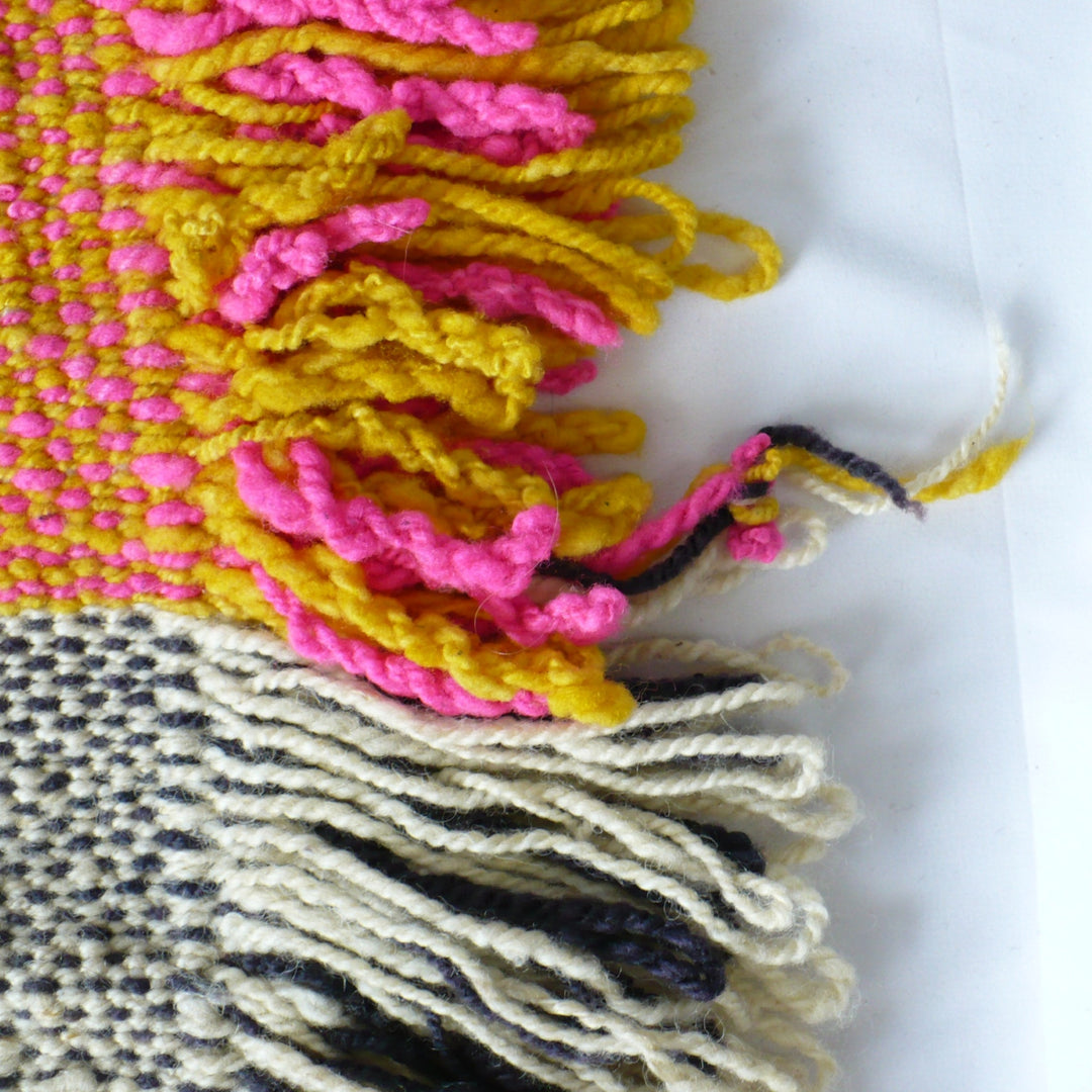1960s Handwoven Mapuche Table Runner: Close-up of a woven textile with thick tassel fringe in bright pink, mustard yellow, cream, and blue on a white background.