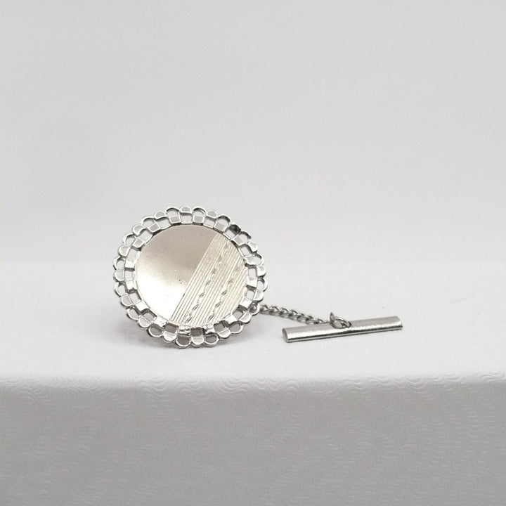 Silver tie pin with scalloped edge on a light gray background