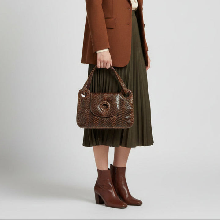 Person holding a Woman in a brown blazer and green skirt holding a1970s Vintage  Luxury leather and Snakeskin Python Purse Handbag on a plain  background wearing a brown coat, green skirt, and brown boots on a light gray background