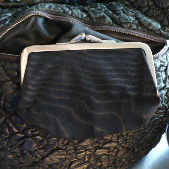 A close-up of a the black moire rayon fabric pouch with a silver metal kiss-lock  coin purse frame.