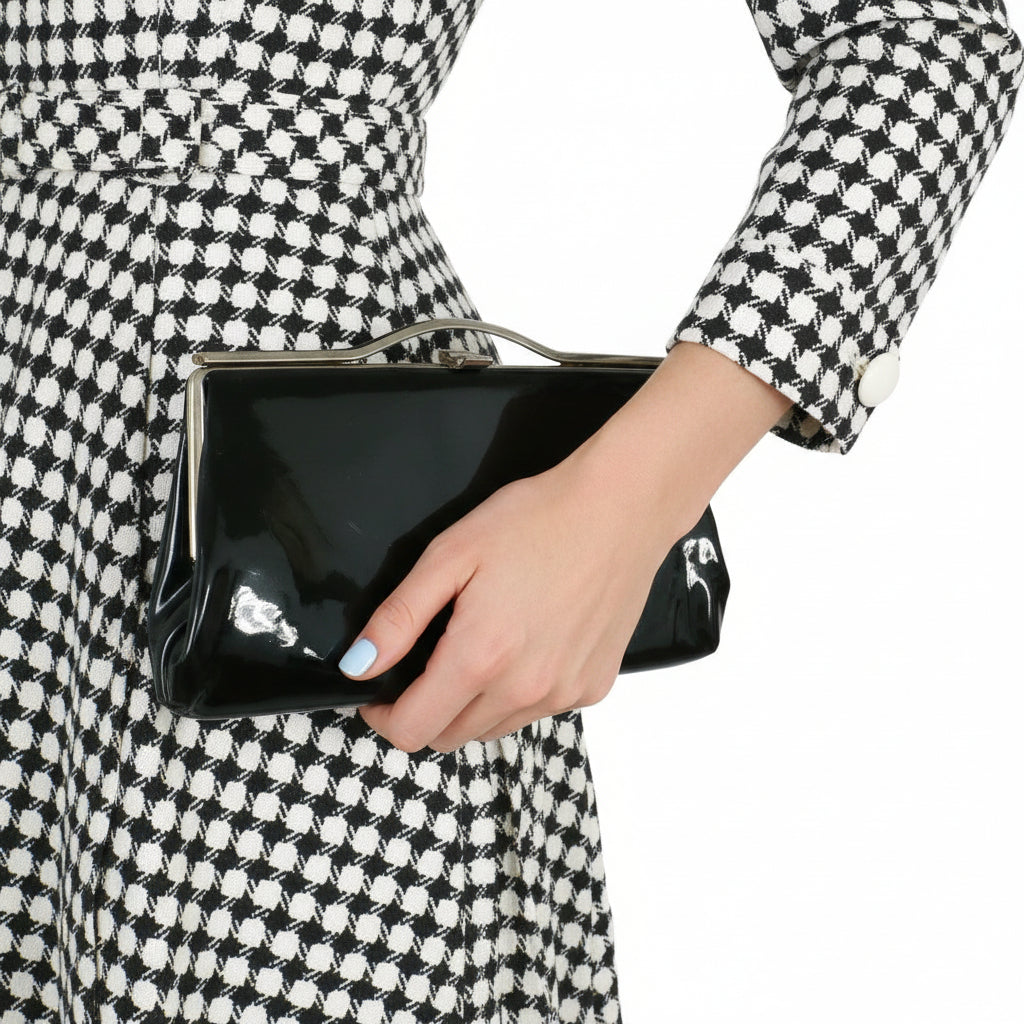 Woman holding a black clutch bag 1960s Vintage Black Patent-look Cutout Handle Long Slender Handbag with a checkered outfit.