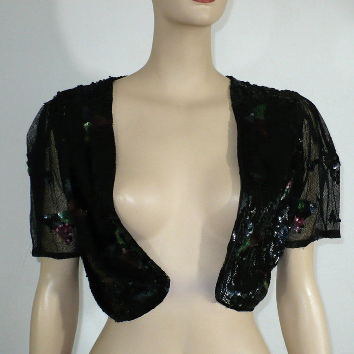 A black sheer mesh bolero shrug with sequined floral details, displayed on a beige mannequin torso, unfastened on a mannequin.