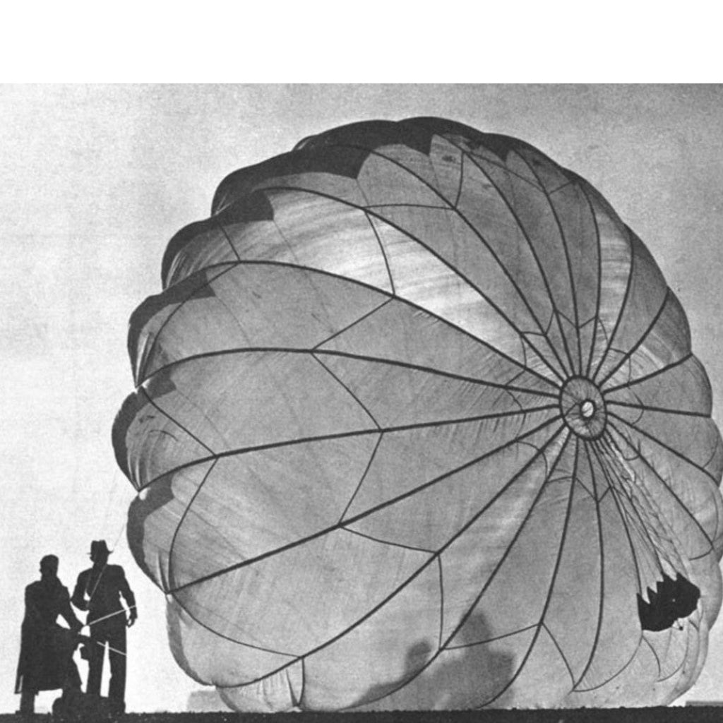 Large sheer parachute with two people standing next to it on a plain background