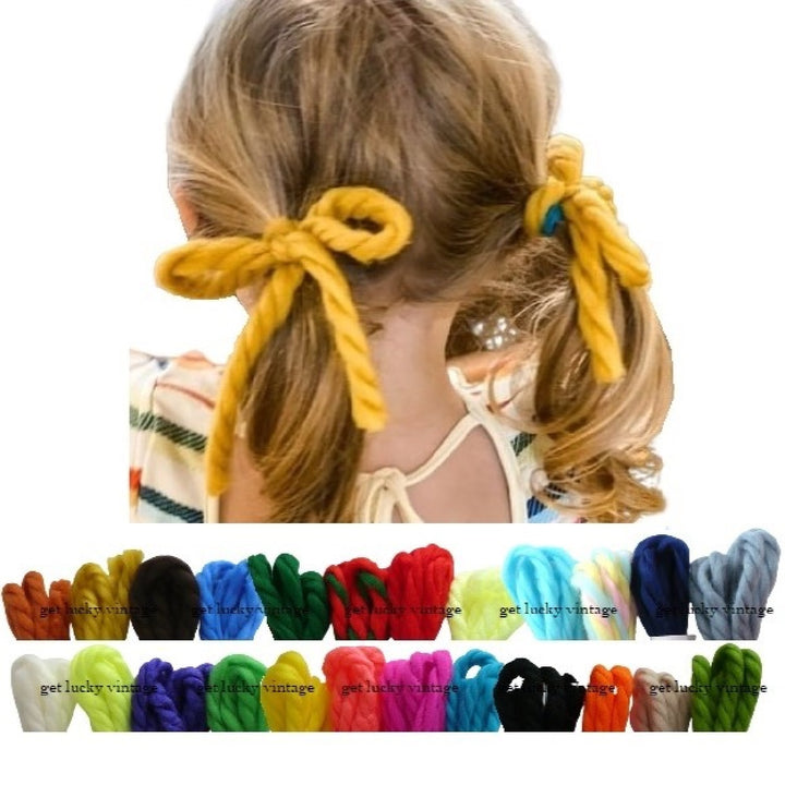 Back of girl's head showing ponytails pigtails with yarn hair ties bows, ribbon color selection at the bottom: white, red yellow, green, blue, pink, orange, purple ginger rust yarn hair ribbons.