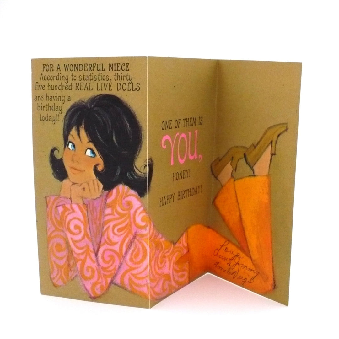A vintage 1960s birthday card for a niece featuring a girl in a pink patterned top and orange pants. Folds out in thirds for an extended view. Text: "According to statistics, thirty-five hundred REAL LIVE DOLLS are having a birthday today!! ONE OF THEM IS YOU, HONEY! HAPPY BIRTHDAY!"