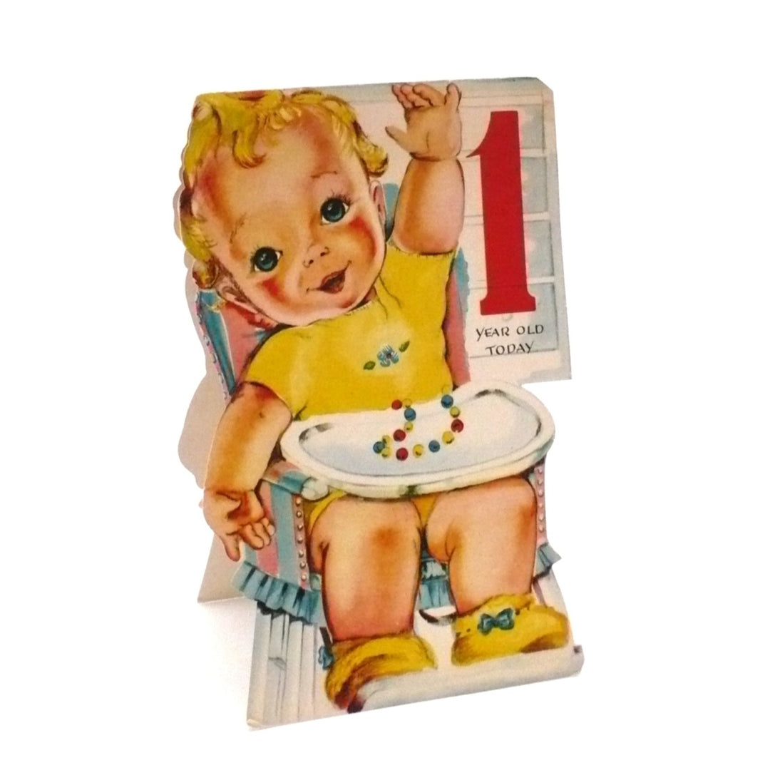 The illustration is a quintessential mid-century "storybook" style. It shows a rosy-cheeked toddler with blonde curls sitting in a white highchair, viewed from behind as they reach a hand toward a wall shelf. The highchair is accented with a blue-and-red striped back cushion and a ruffled blue skirt at the base. The die-cut edges follow the silhouette of the baby and the chair, creating a custom shaped feel when closed.