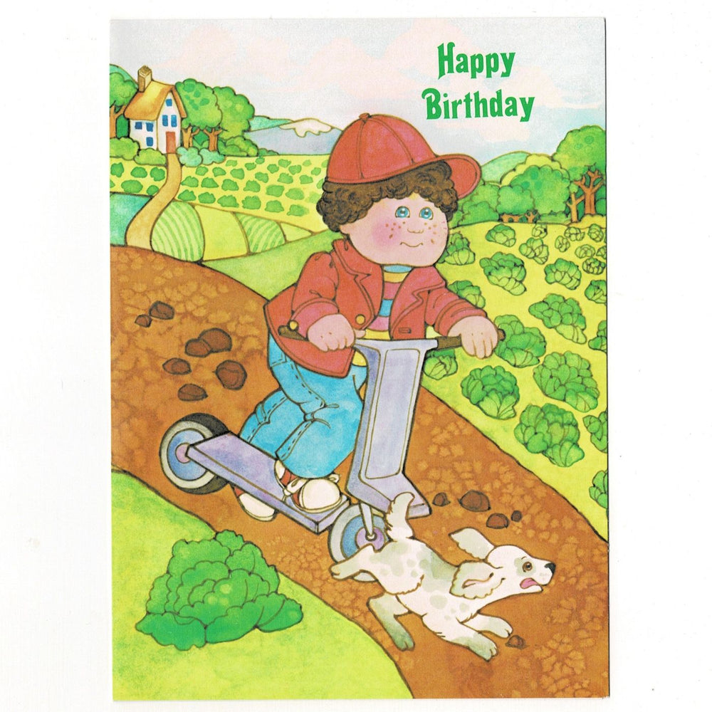 This authentic 1980s card features a classic Cabbage Patch Kids illustration by Current. The scene depicts a "Kid" in a red jacket and baseball cap riding a lavender scooter down a dirt path, accompanied by a playful, spotted puppy. In the background, the rolling green hills of the "Patch" are visible, dotted with cabbages and a small cottage.