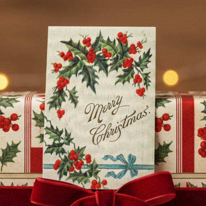 1907 Blue Bow Traditional Vintage Antique Christmas Postcard, set against a blurred gift-wrapped background.