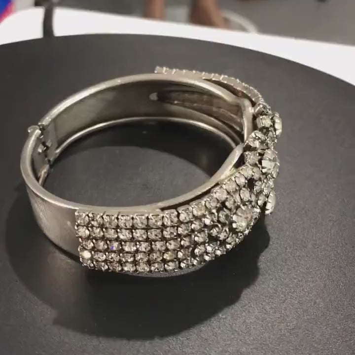 Vintage clamper bracelet turns on a display platform to show the prong set crystal rhinestones sparkle as it moves. 