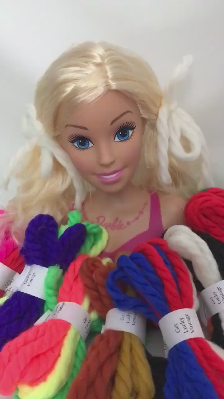 Holiday themed bundles of vintage yarn hair ties surrounding a toy Barbie bust wearing a pair.