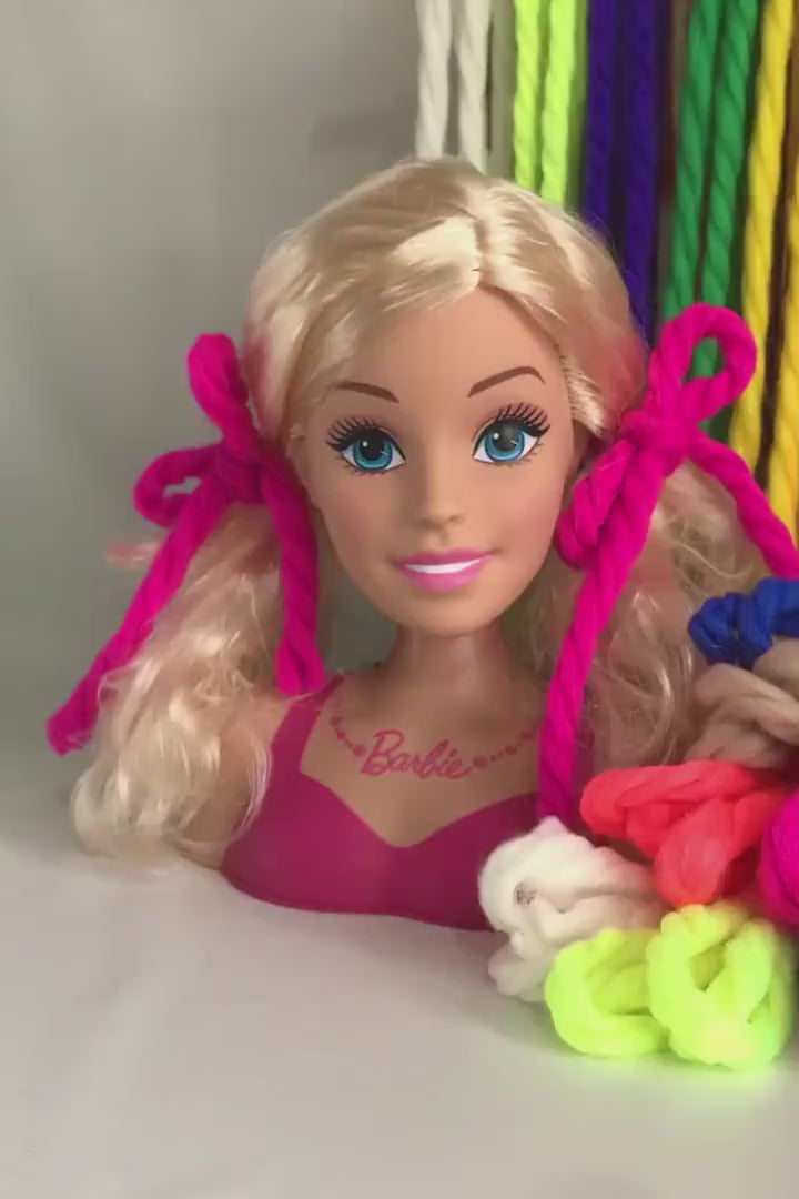 Yarn hair ties behind and next to Barbie styling bust wearing yarn hair ties.