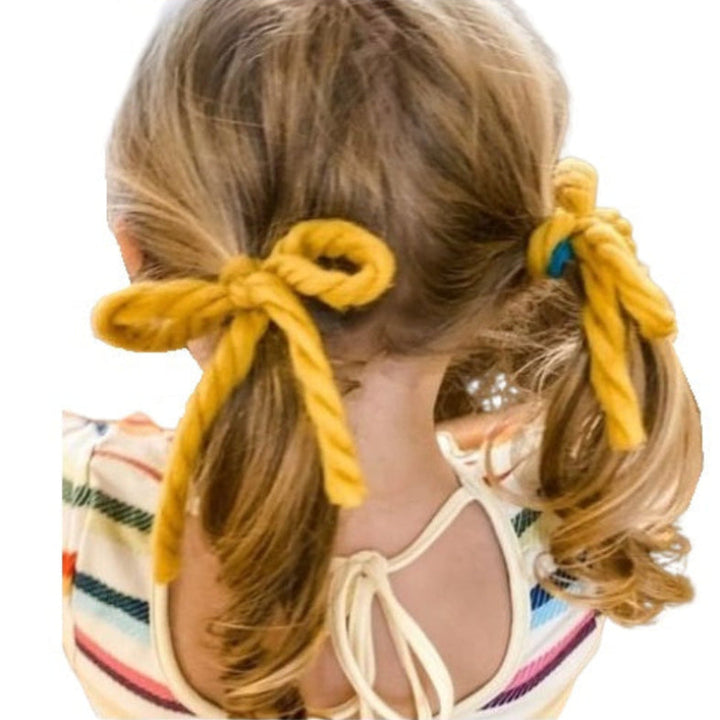 Child with blonde hair styled in two ponytails tied with vintage yarn hair ribbons on a white background.